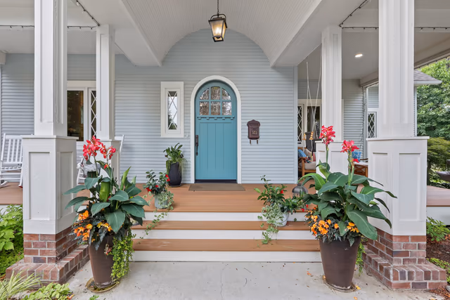 Blue arched front door framed by porch columns and flowering planters
