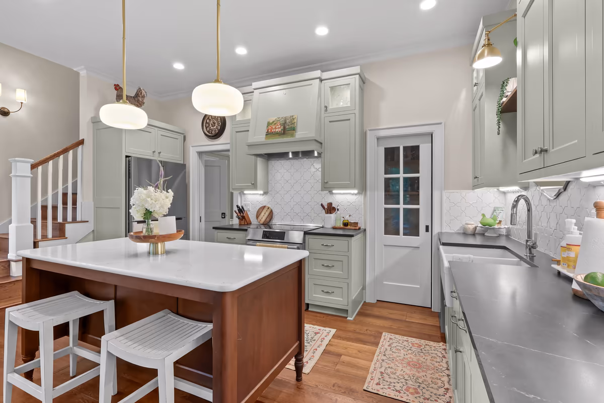 Sink-side view of the sage-green kitchen with wood floors