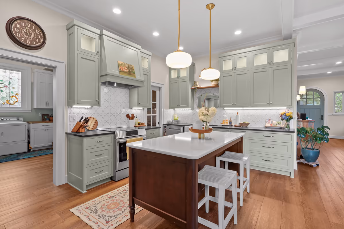 Sage-green kitchen with an island, globe pendants, and wood floors