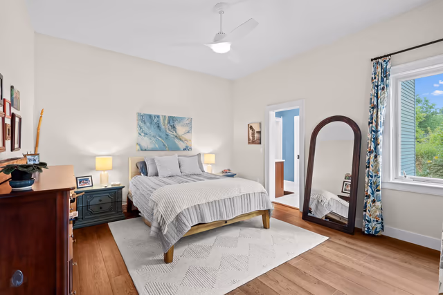 Bright bedroom with neutral bedding, a floor mirror, and wood floors