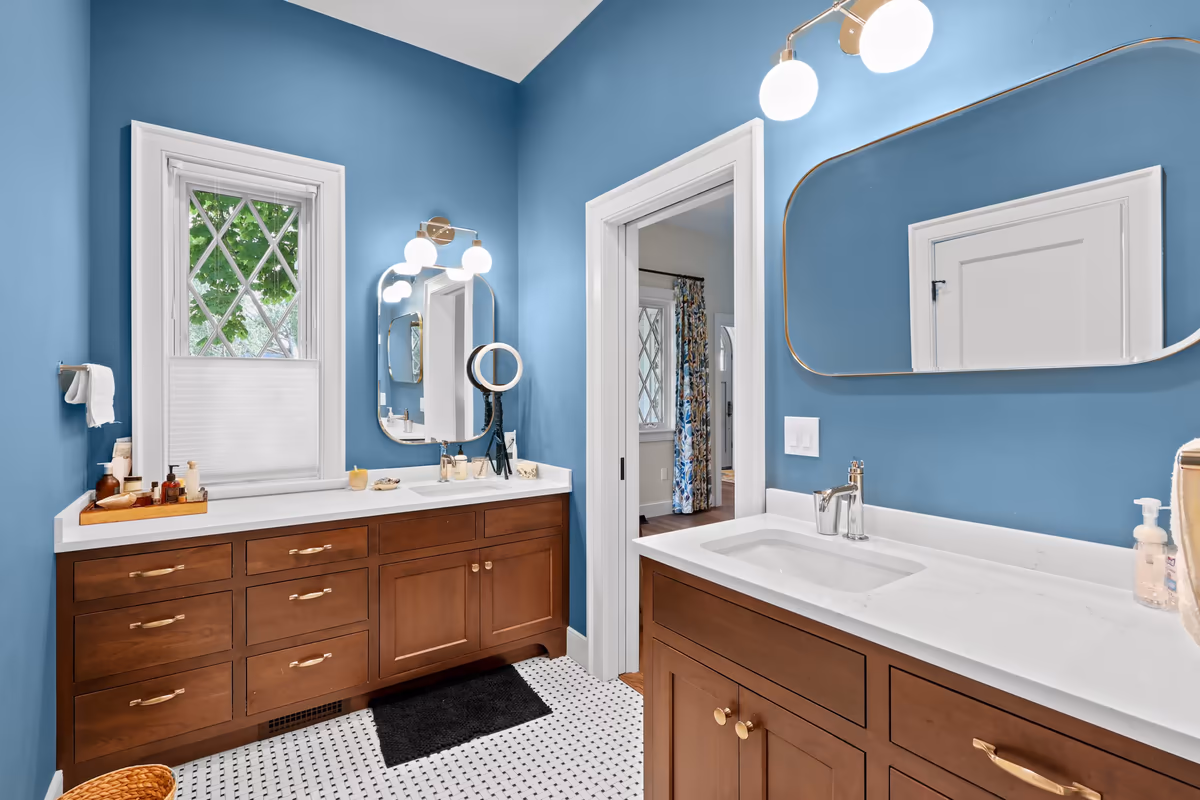 Blue bathroom with wood vanities and rounded brass-framed mirrors
