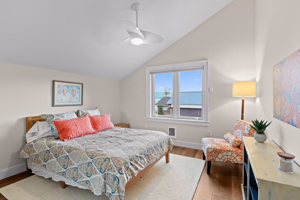 Bedroom with colorful bedding, a patterned accent chair, and wood floors