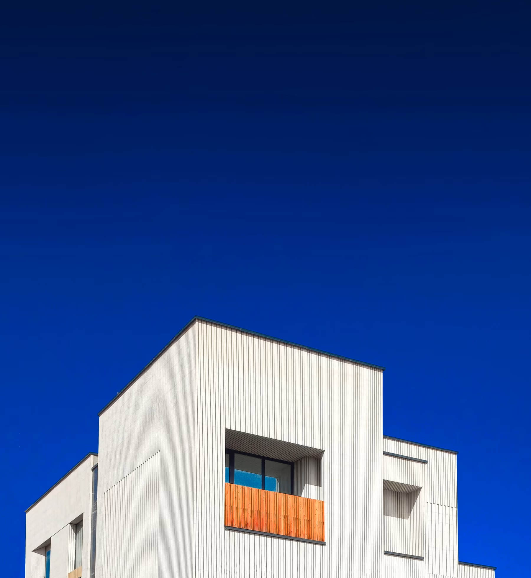 White geometric residence against a deep blue sky with a single warm balcony detail